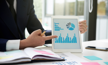 Person analyzing asset tracking best practices with bar and pie charts on a tablet, surrounded by notes and documents.