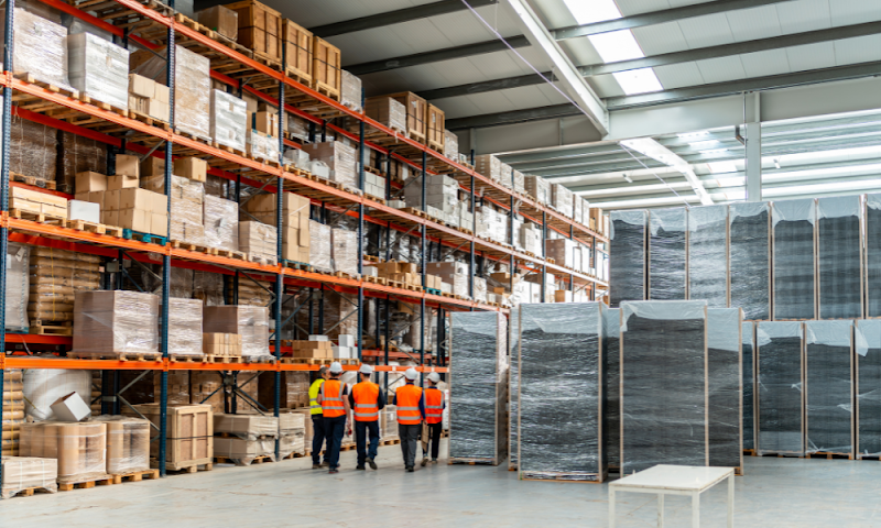 Large warehouse with workers inspecting inventory racks, illustrating warehouse system management for large-scale storage operations.